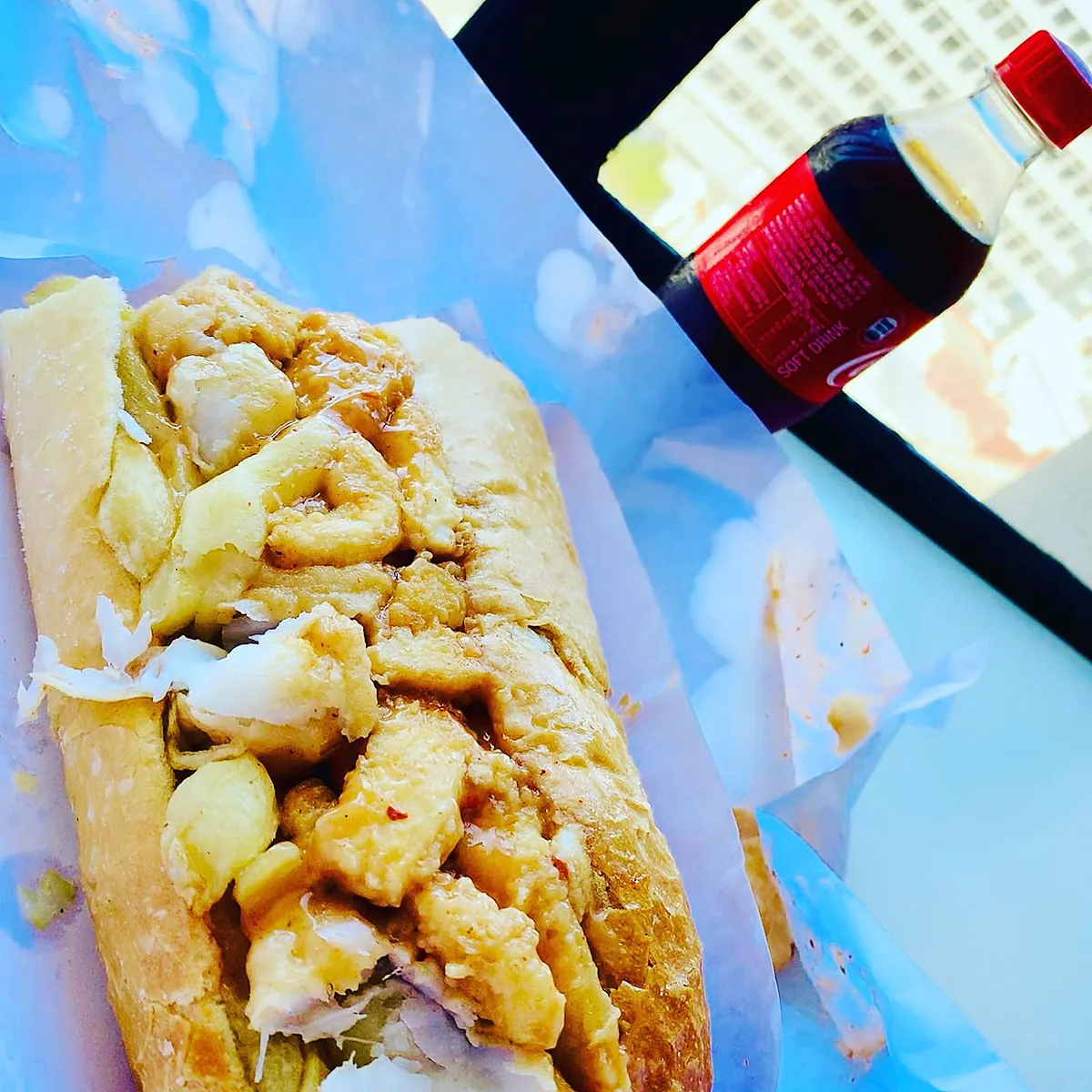 A calamari Gatsby on white paper next to a bottle of Coke.