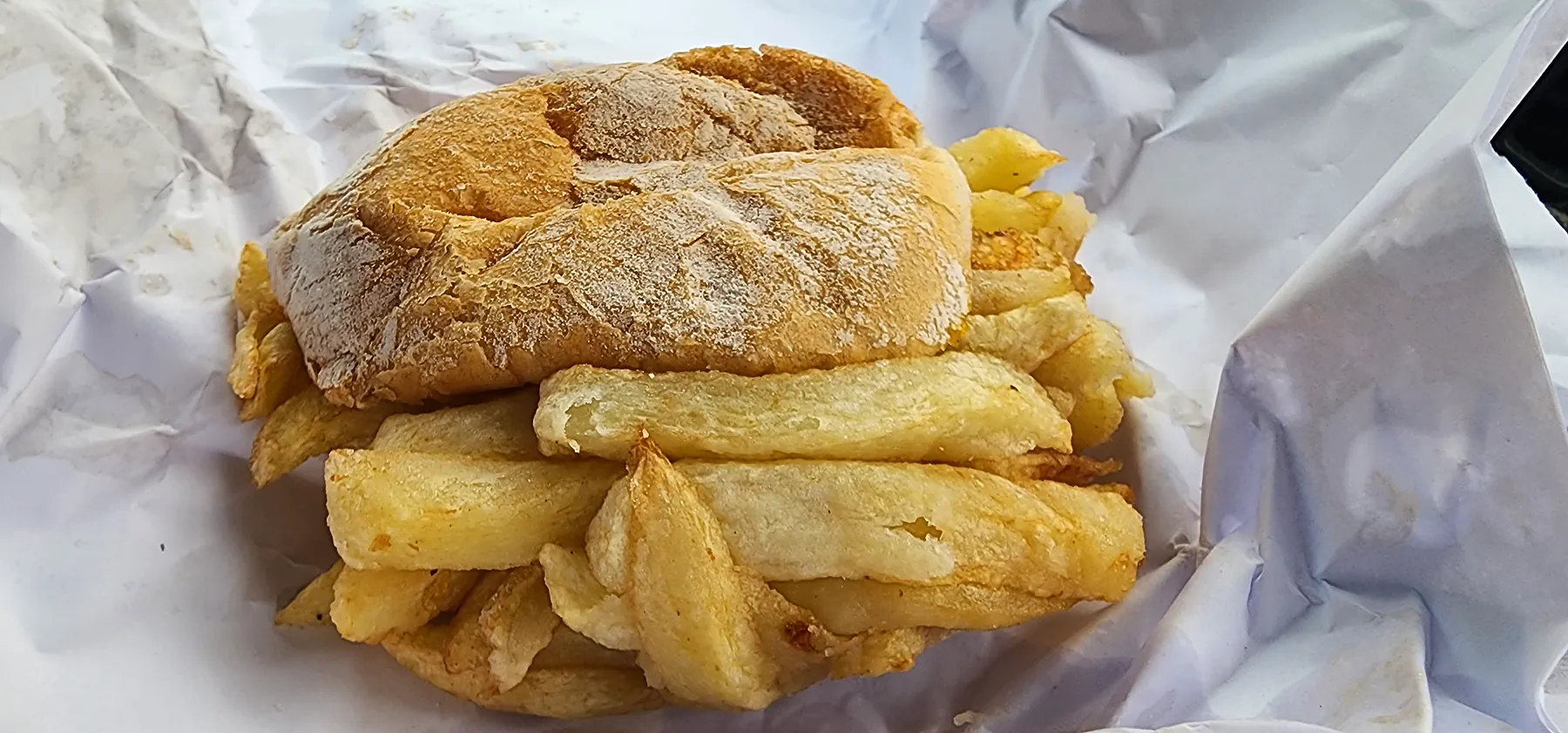Battered fish and slap chips on a crusty roll, wrapped in white paper.