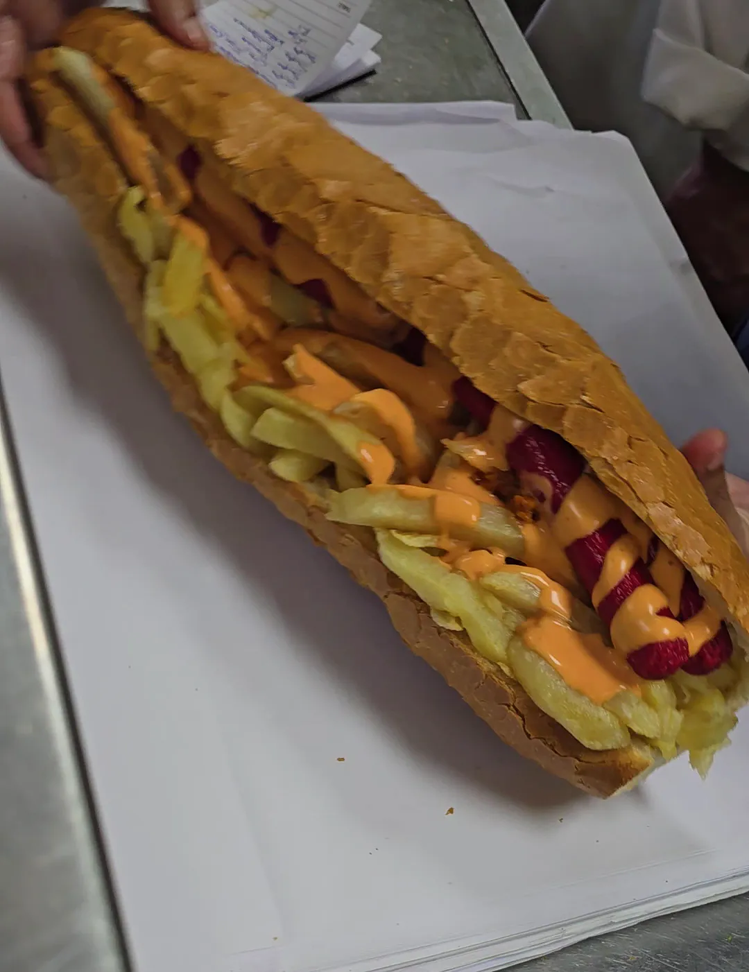 A polony Gatsby with chips and sauce, cut open on paper.