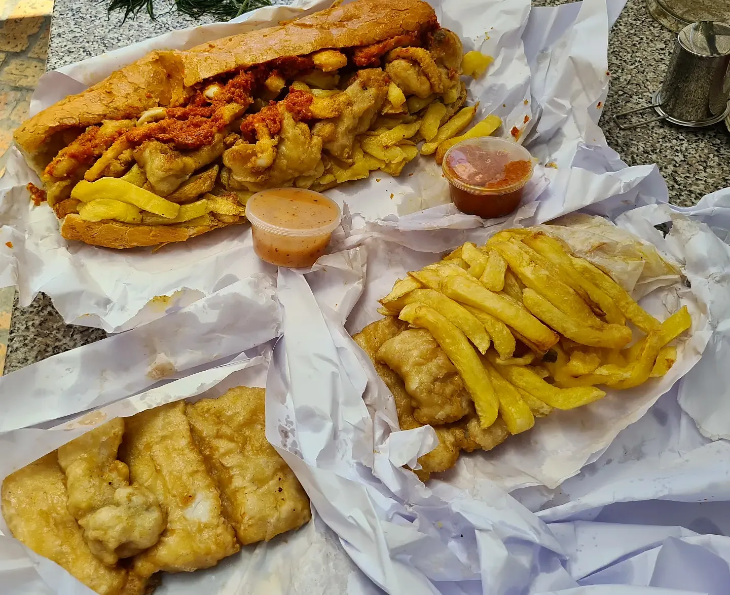 A Gatsby, fish and chips and dipping sauces spread out on paper.